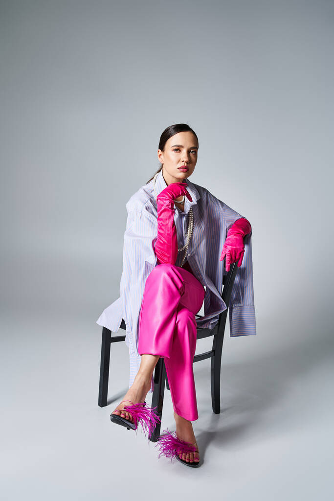 Pewna siebie brunetka dziewczyna w różowych rękawiczkach, pióro buty i stylowe spodnie, siedzi na krześle - Zdjęcie, obraz