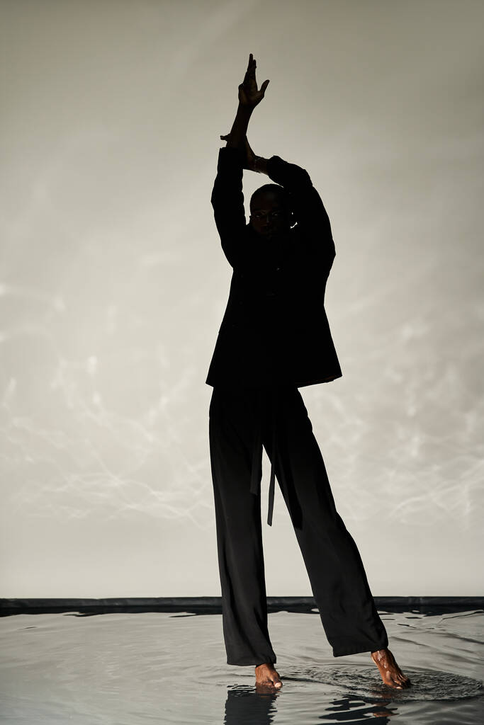 silueta stylového afrického Američana pózujícího bosý v obleku na vodnatém pozadí ve stínu - Fotografie, Obrázek