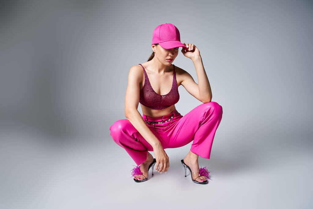 Fancy brunette woman in red top and pink trousers touching stylish cap with one hand - Photo, Image