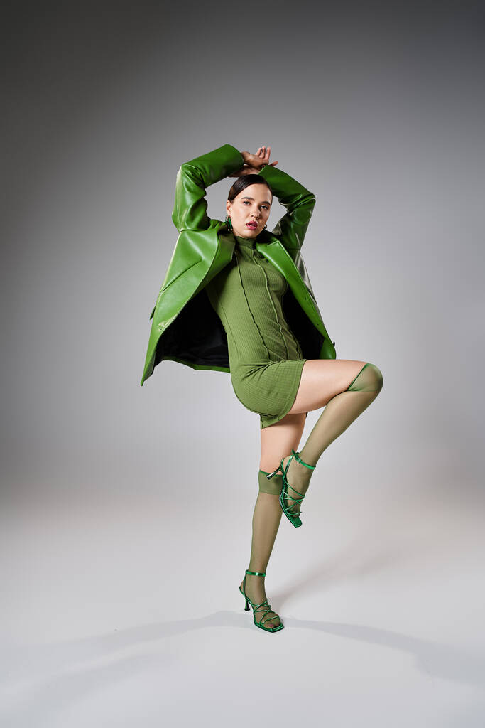 Brune avant-gardiste dans un look tendance vert total dansant sur fond gris en studio - Photo, image