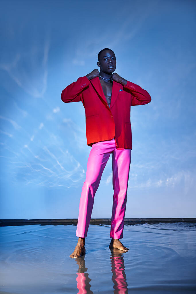 スタイリッシュなアフリカ系アメリカ人男性をピンクのズボンと赤いブレーザーで魅了し,青い水色の背景にポーズ - 写真・画像