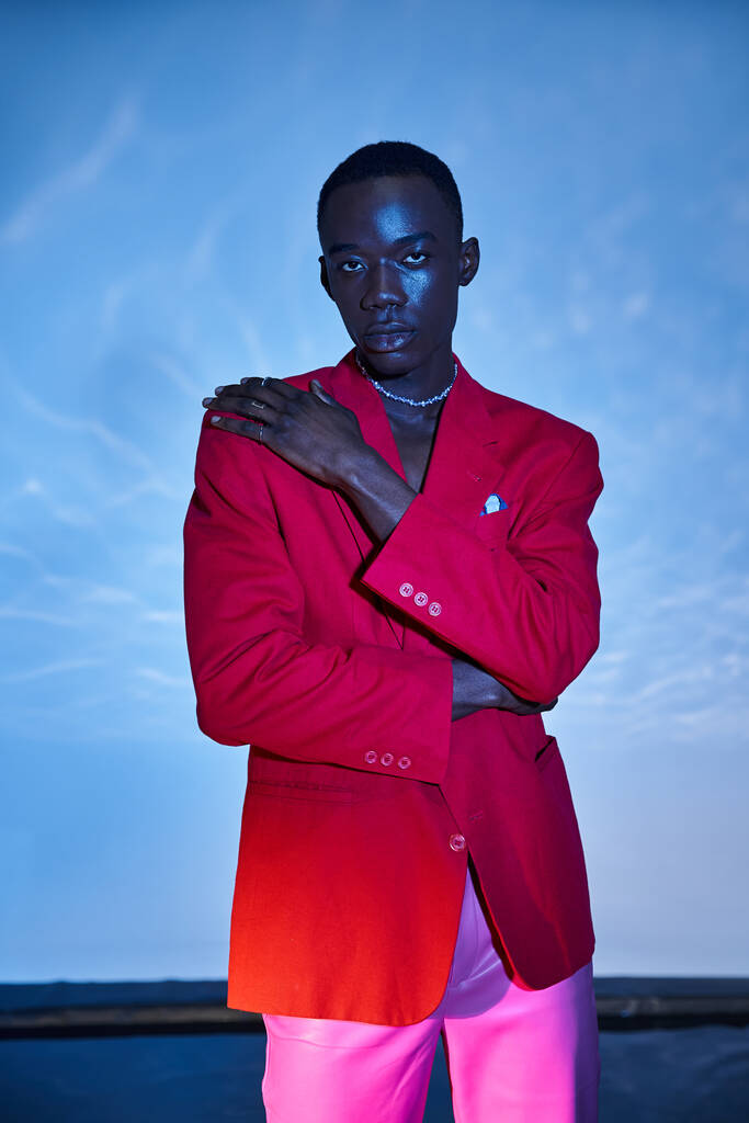 Çekici, Afro-Amerikalı, pembe pantolonlu, kırmızı ceketli, mavi arkaplanda poz veren adam. - Fotoğraf, Görsel