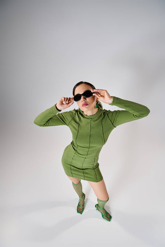 Вид зверху на жінку в зеленому міні-сукні і шкарпетках на колінах, торкаючись її окулярів обома руками - Фото, зображення