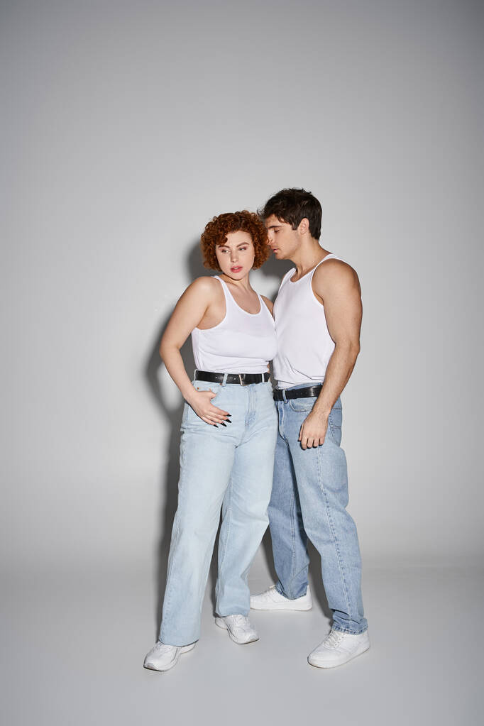 appealing sexy couple in blue jeans posing together lovingly on gray background, relationship - Photo, Image