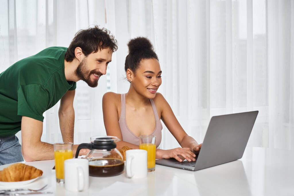 Neşeli, güzel, ırklar arası bir çift laptopta film seyrediyor evde kahvaltıları sırasında. - Fotoğraf, Görsel