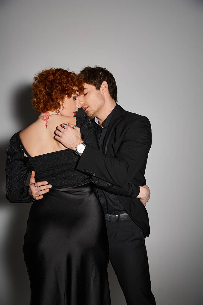 verführerisch sexy Paar in schwarzen eleganten Kleidern küssen und umarmen sich liebevoll auf grauem Hintergrund - Foto, Bild
