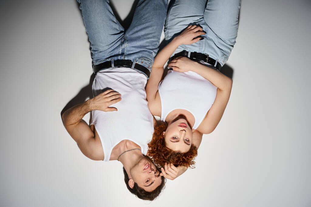 заманчивые мужчина и женщина в синих джинсах лежат на полу вместе и смотрят в камеру, сексуальная пара - Фото, изображение