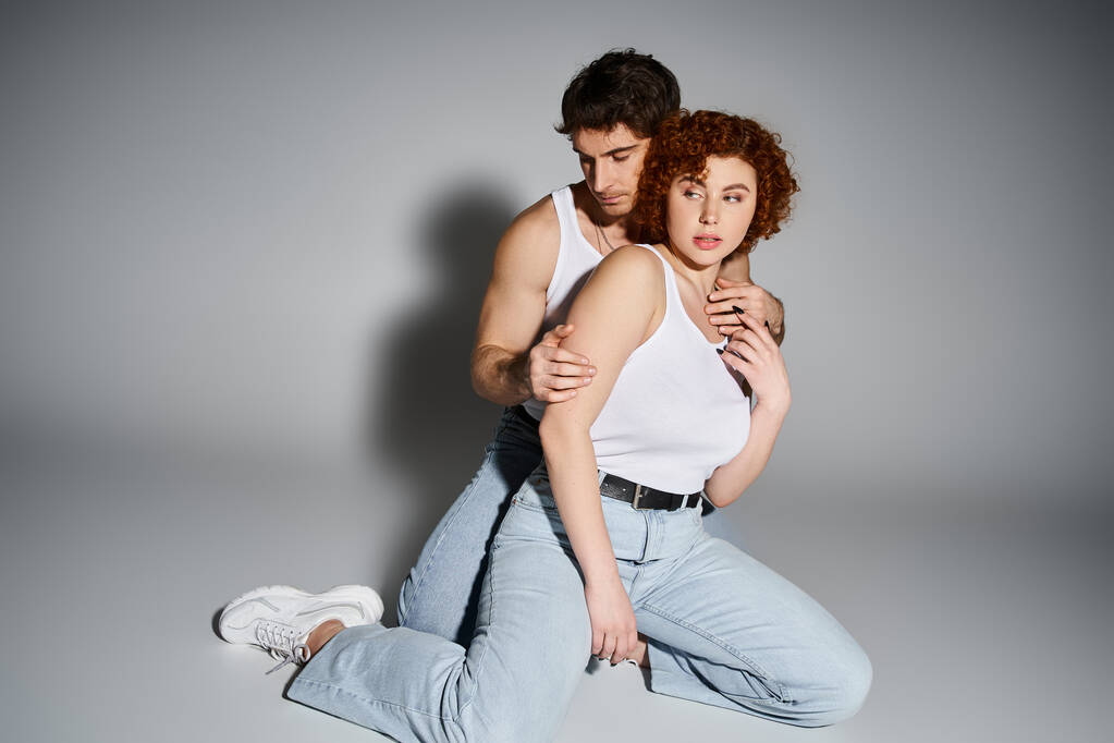 соблазнительные мужчина и женщина в синих джинсах сидят на полу вместе и обнимаются теплой, сексуальной парой - Фото, изображение