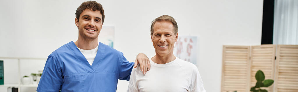 joyeux médecin attrayant et son patient joyeux mature posant ensemble et souriant à la caméra, bannière - Photo, image