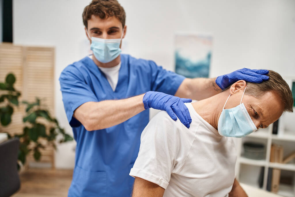 リハビリテーション中に患者が伸びるのを助けるマスクと手袋の勤勉な医師 - 写真・画像