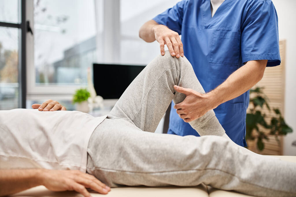 обрізаний вид на відданого лікаря в блакитному халаті, що розтягує м'язи свого зрілого пацієнта в лікарні - Фото, зображення