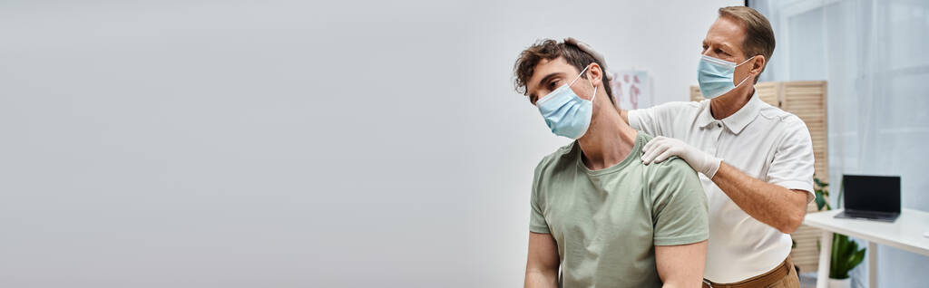 attractive mature doctor with mask helping his patient to rehabilitate in hospital ward, banner - Photo, Image