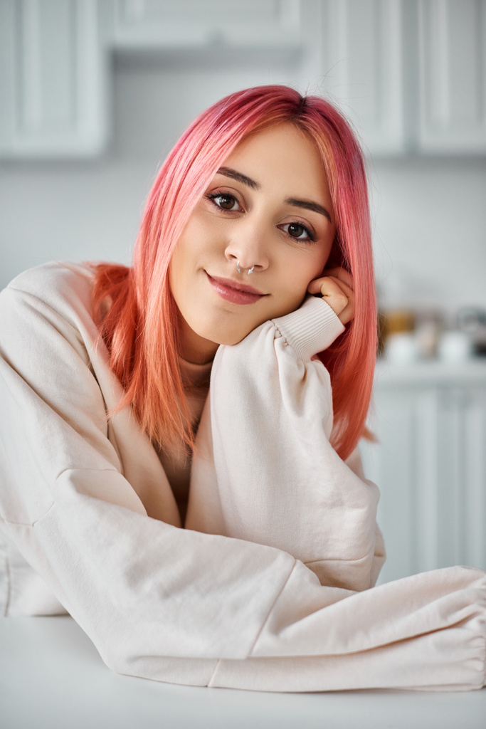 красива молода жінка з рожевим волоссям в повсякденному вбранні позує на кухні і посміхається на камеру - Фото, зображення