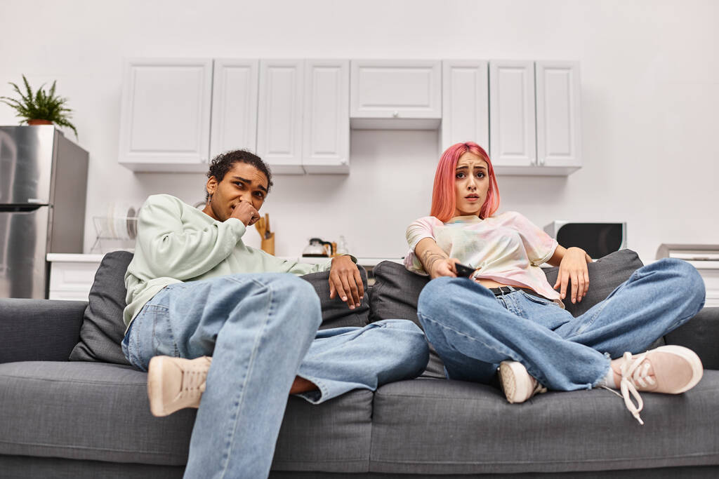 rémült multikulturális pár otthonos otthonban horror filmeket néz otthon a nappaliban - Fotó, kép