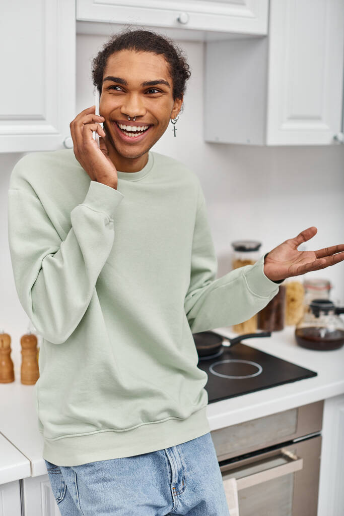 attractive jolly african american man in casual green sweater talking by phone and looking away - Photo, Image