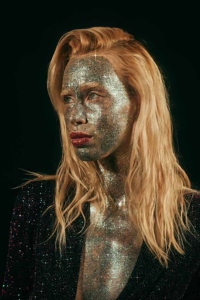 portrait of blonde woman with green eyes and glitter on face and body posing on black backdrop - Photo, Image