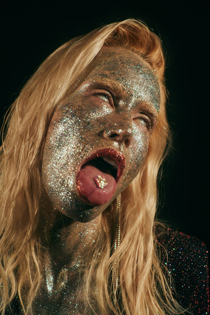 retrato de mujer rubia provocativa con brillo en la cara y el cuerpo rodando los ojos sobre fondo negro - Foto, imagen