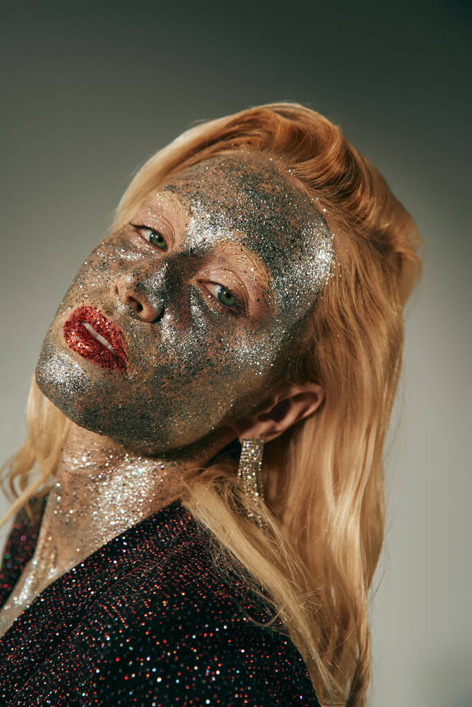 verleidelijke jonge vrouw met groene ogen en glitter over lichaam en gezicht poseren op grijze achtergrond - Foto, afbeelding