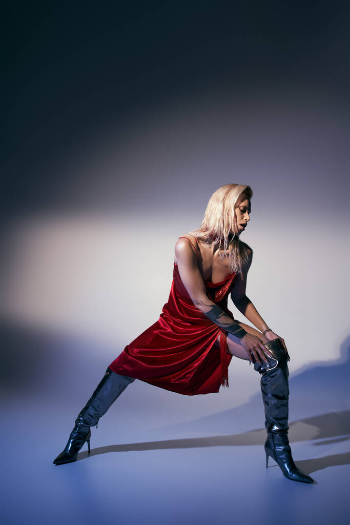 красивая стильная женская модель в красном платье и кожаных туфлях позирует в движении на сером фоне - Фото, изображение