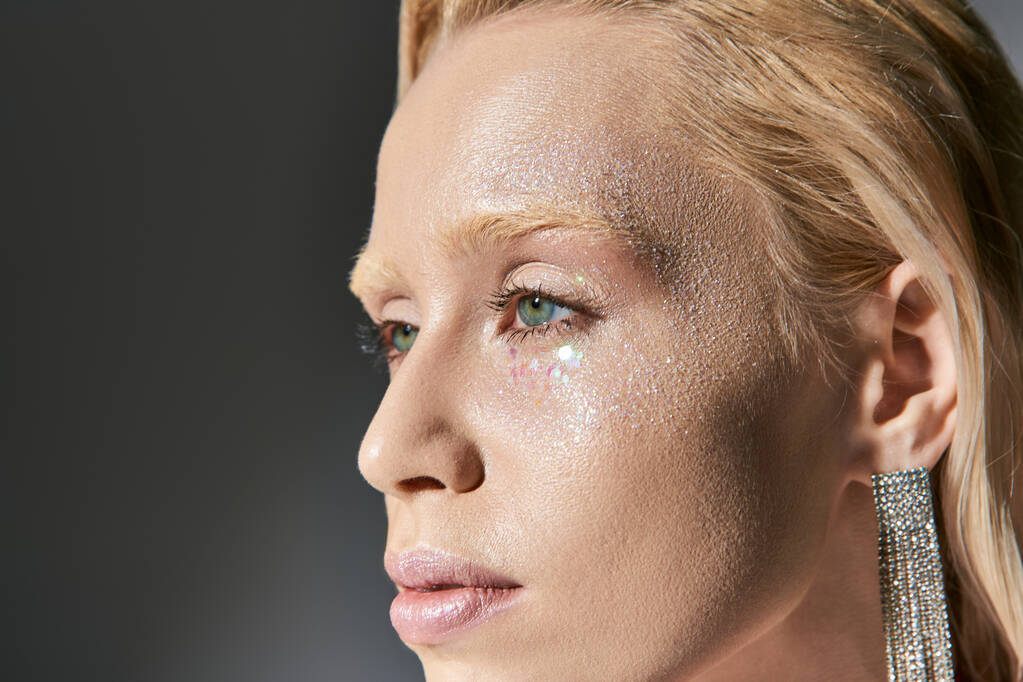 πορτρέτο της ελκυστική γυναίκα με σκουλαρίκια και πράσινα μάτια που θέτουν σε γκρι φόντο και κοιτάζοντας μακριά - Φωτογραφία, εικόνα