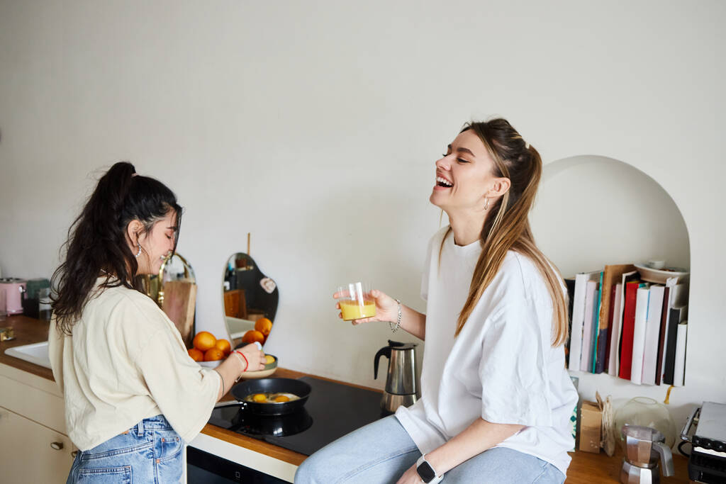щаслива молода жінка готує сніданок біля смішної дівчини з апельсиновим соком, пара ЛГБТ - Фото, зображення