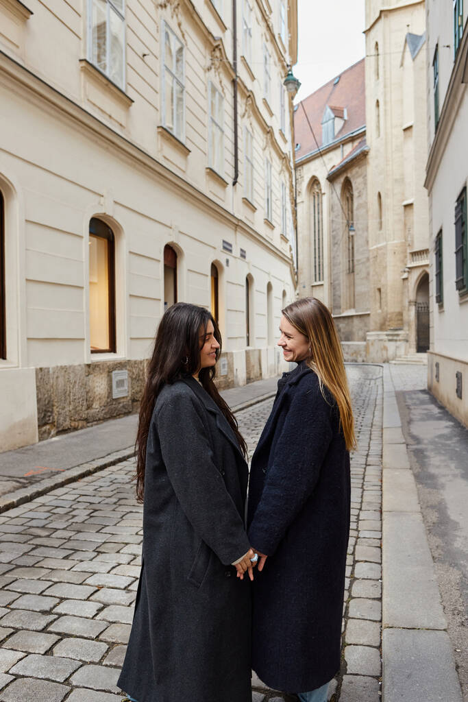 feliz joven pareja lesbiana en ropa de abrigo de moda de la mano durante el paseo en la ciudad europea, lgbt - Foto, imagen