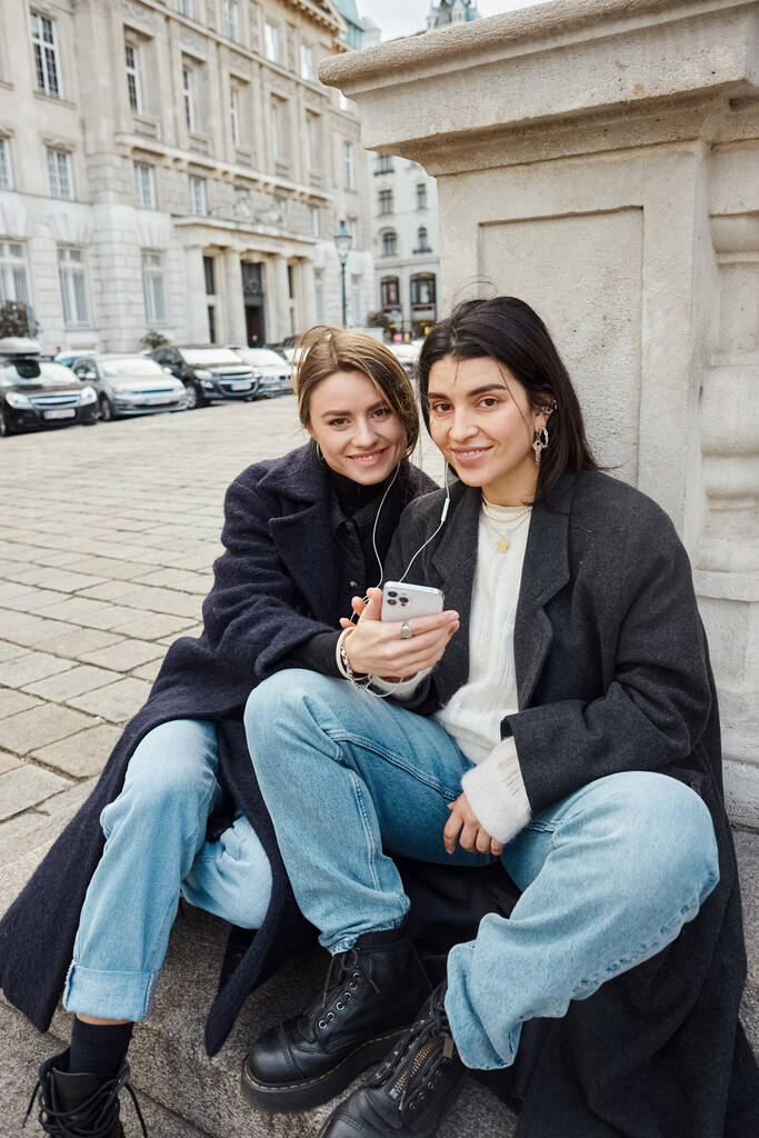 Mutlu genç lezbiyen çift Viyana 'da birlikte otururken kulaklıkla müzik dinliyor. - Fotoğraf, Görsel