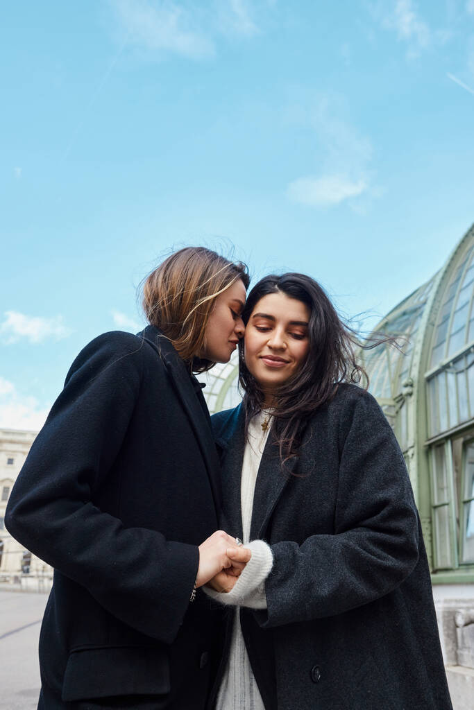 любляча пара lgbt в пальто тримає руки, стоячи біля Пальменгауза у Відні на фоні - Фото, зображення