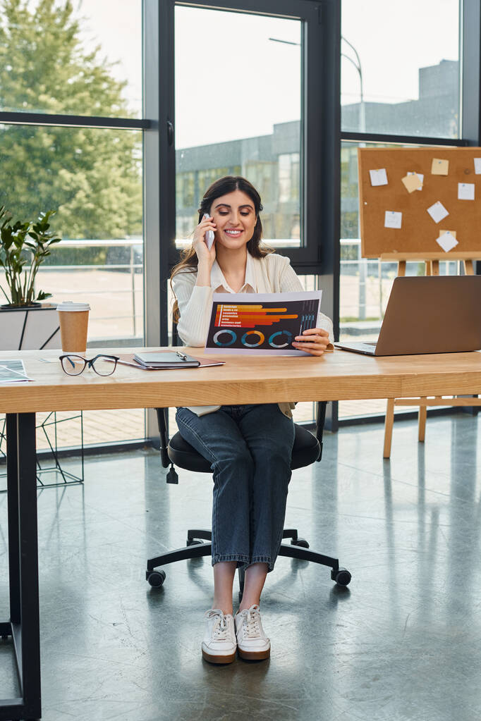 Egy fókuszált üzletasszony ül egy asztalnál diagramokkal egy modern irodai környezetben, megtestesítve az üzlet és a tanulás fogalmát. - Fotó, kép