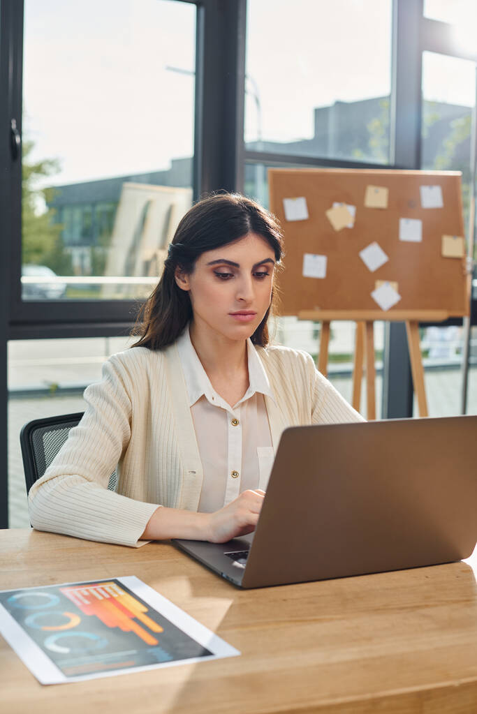 Бізнес-леді в сучасному офісі сидить за столом, орієнтований на використання ноутбука для роботи. - Фото, зображення