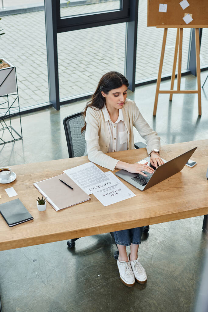 Деловая женщина в современном офисе, сосредоточенная на ноутбуке за столом, погруженная в мир предпринимательства. - Фото, изображение