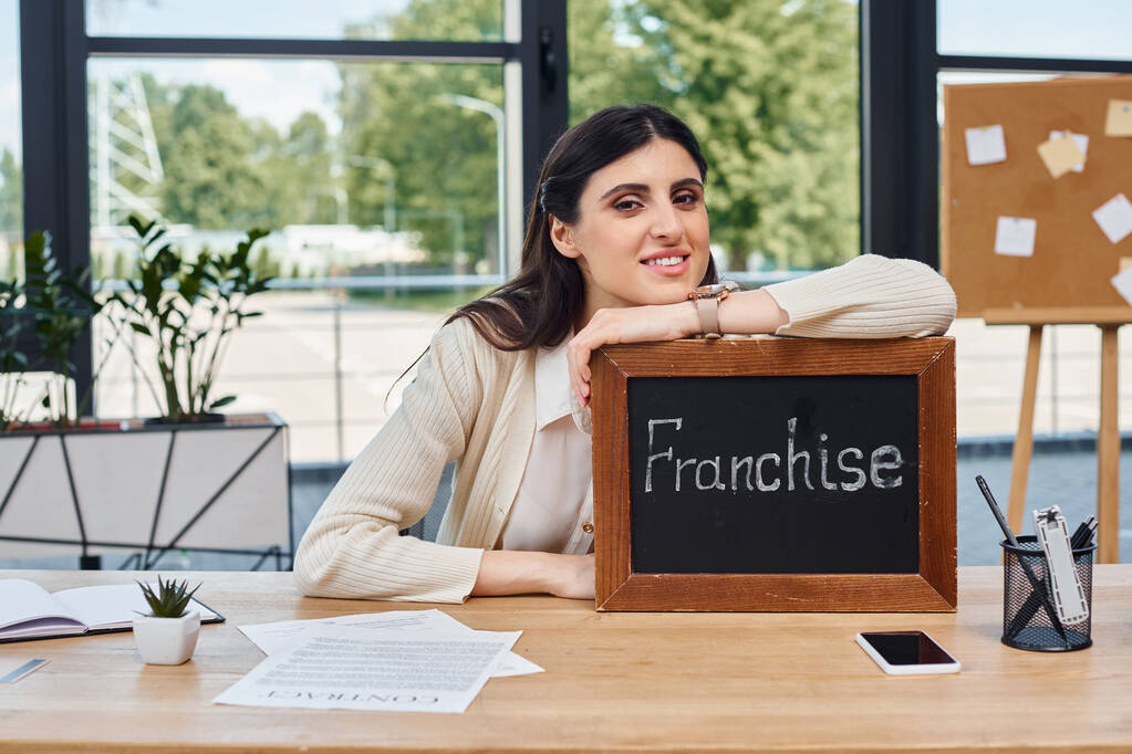A businesswoman sits at a modern desk, prominently displaying a sign as a symbol of her entrepreneurial endeavors. - Photo, Image