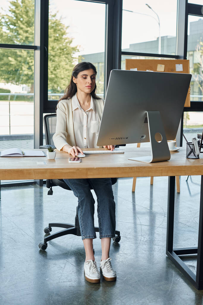 Сосредоточенная бизнесвумен сидит за сонным столом, окруженная экраном компьютера, воплощая современную концепцию франшизы. - Фото, изображение