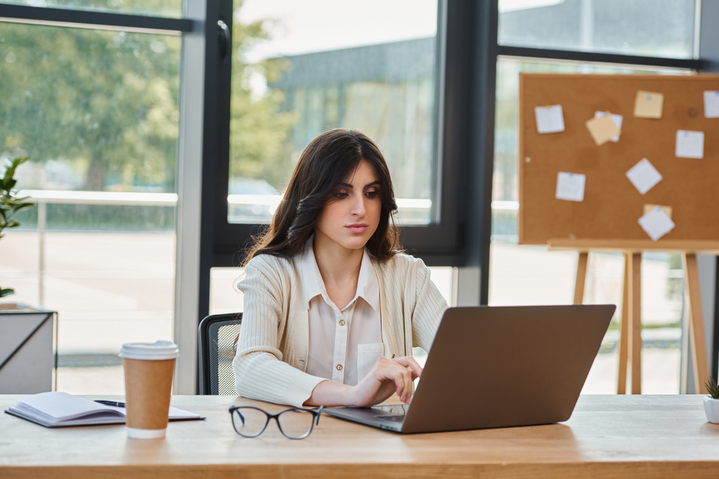 Uma mulher de negócios imersa em um laptop em sua mesa de escritório moderna, criando estratégias para um empreendimento de franquia. - Foto, Imagem