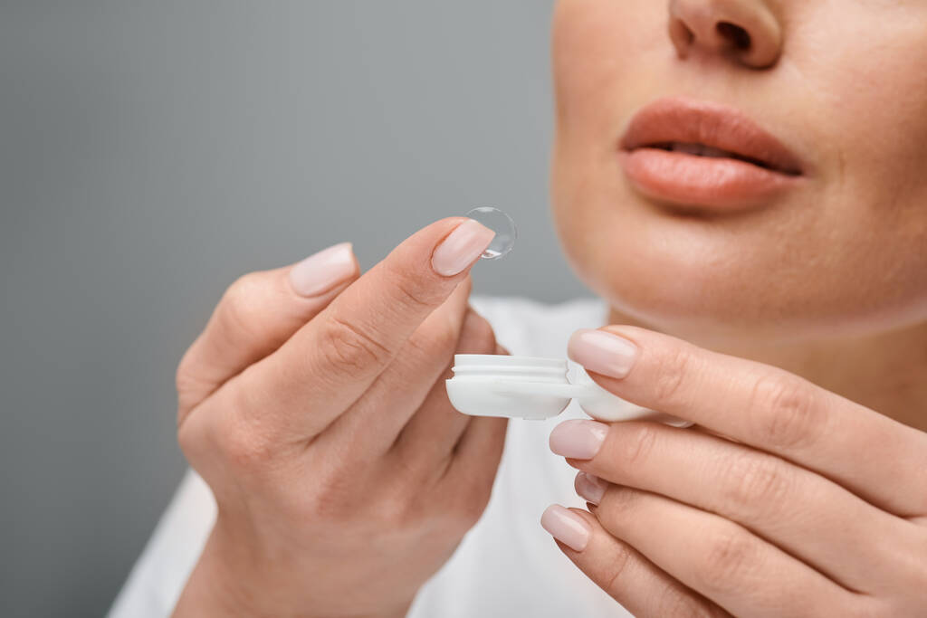 oříznutý pohled na koncentrovaný ženský model nošení kontaktních čoček opatrně na šedém pozadí - Fotografie, Obrázek