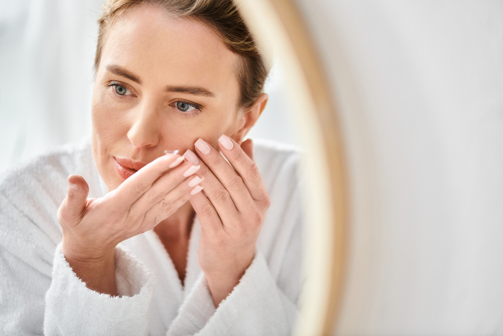 hermosa mujer en blanco cómodo albornoz usando sus lentes de contacto cerca del espejo en el baño - Foto, Imagen