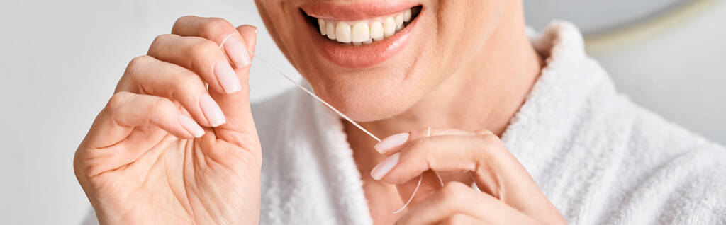 vista recortada de mujer alegre en albornoz limpiando sus dientes con hilo dental en el baño, pancarta - Foto, imagen