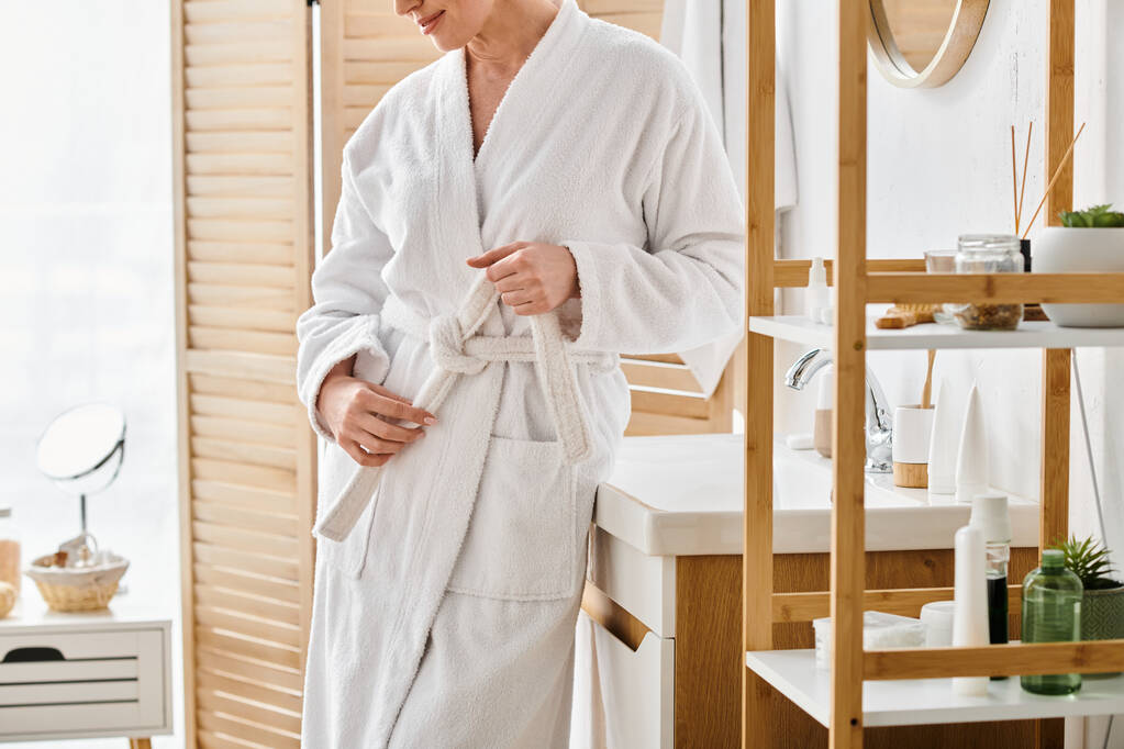 обрезанный вид на взрослую женщину в удобном халате позирует в своей просторной ванной комнате дома - Фото, изображение
