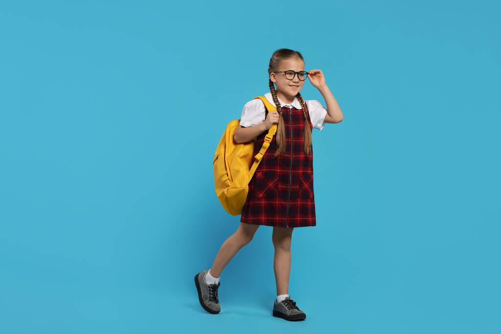 Açık mavi arka planda sırt çantalı, gözlüklü mutlu kız öğrenci. - Fotoğraf, Görsel