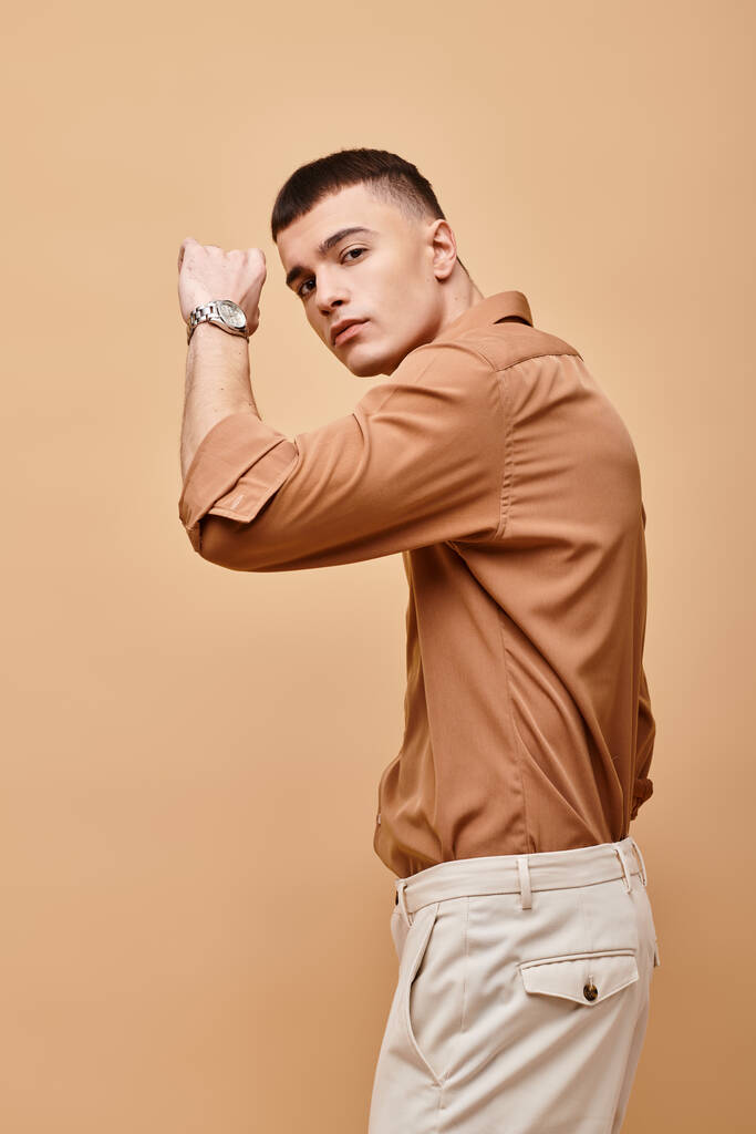 Retrato de moda de hombre guapo en camisa beige con la mano cerca de la cara sobre fondo beige - Foto, Imagen
