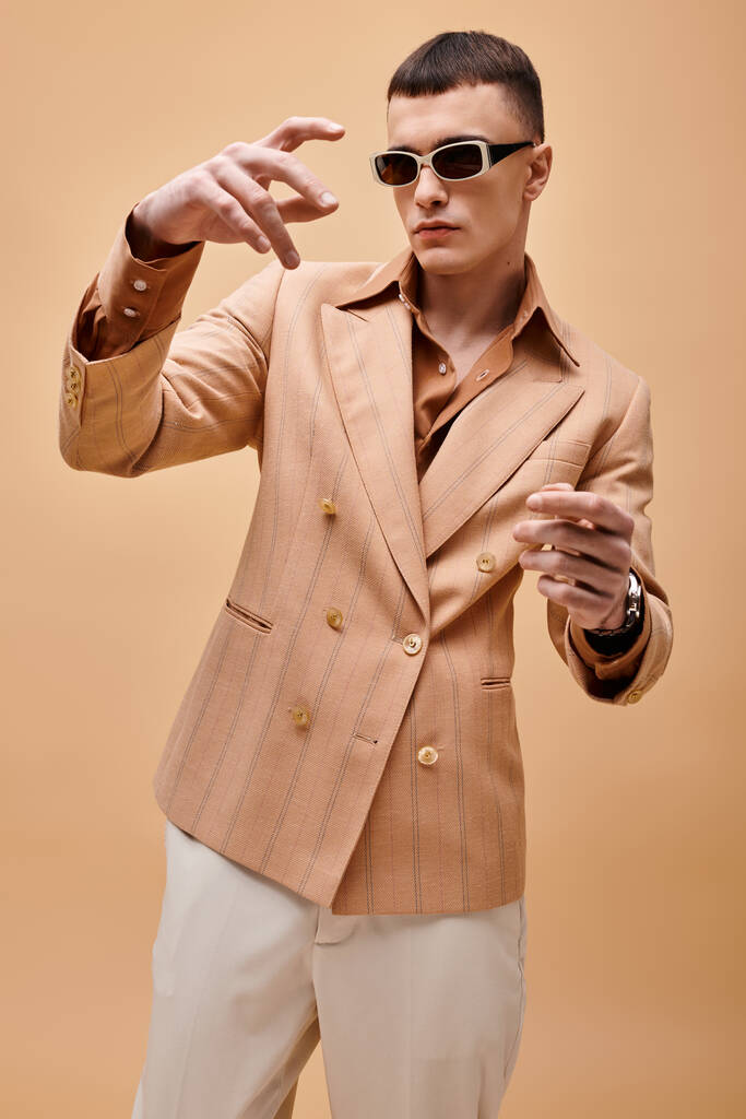 Retrato de hombre guapo con estilo en chaqueta beige manos en movimiento sobre fondo beige melocotón - Foto, imagen