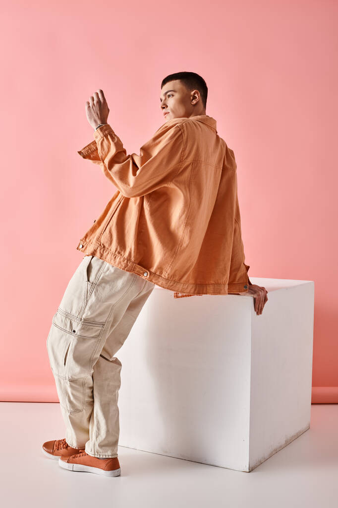 Εικόνα μόδας του κομψού άνδρα σε μπεζ πουκάμισο, παντελόνι και μπότες σε λευκό κύβο σε ροζ φόντο - Φωτογραφία, εικόνα