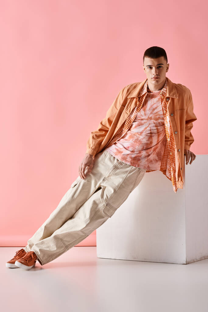 Полная длина изображения стильного человека в бежевой рубашке, брюках и сапогах на белом кубе на розовом фоне - Фото, изображение