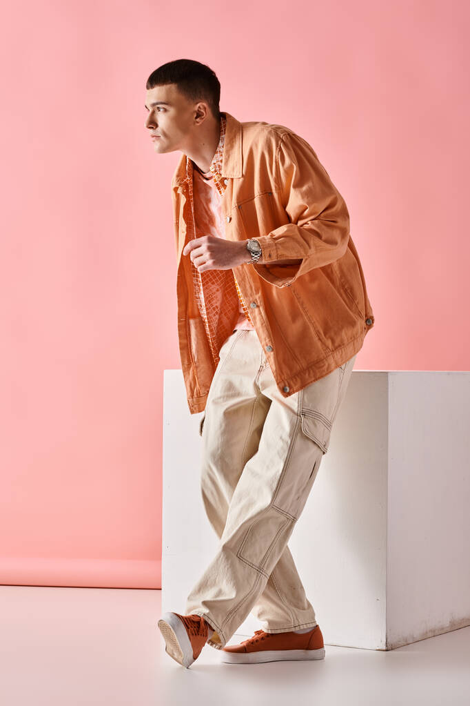 Imagem de comprimento total do homem elegante na camisa bege, calças e botas no cubo branco no fundo rosa - Foto, Imagem