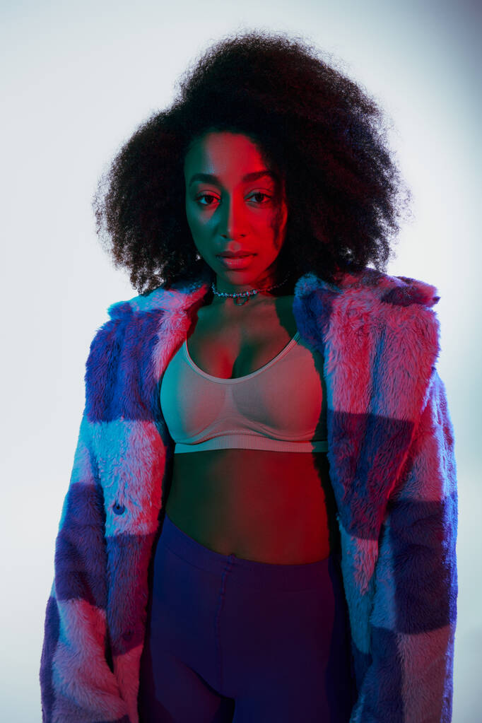 alluring african american woman in bra and faux fur looking at camera surrounded by lights, fashion - Photo, Image
