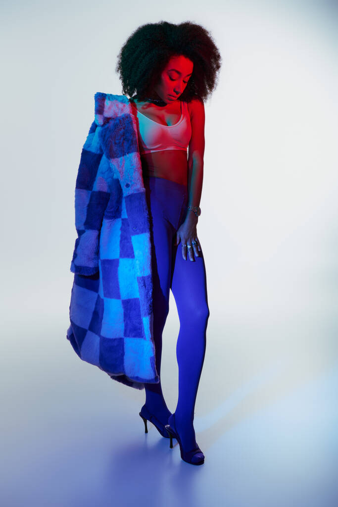 σαγηνευτικό κομψό αφρικανικό αμερικανικό θηλυκό μοντέλο στη μόδα faux γούνα αναζητούν τρόπο στα φώτα - Φωτογραφία, εικόνα