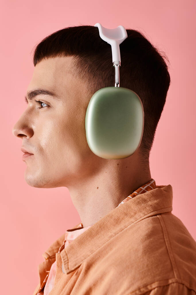 Seitenansicht eines stilvollen Mannes mit drahtlosen Kopfhörern, der Musik auf rosa Hintergrund hört - Foto, Bild