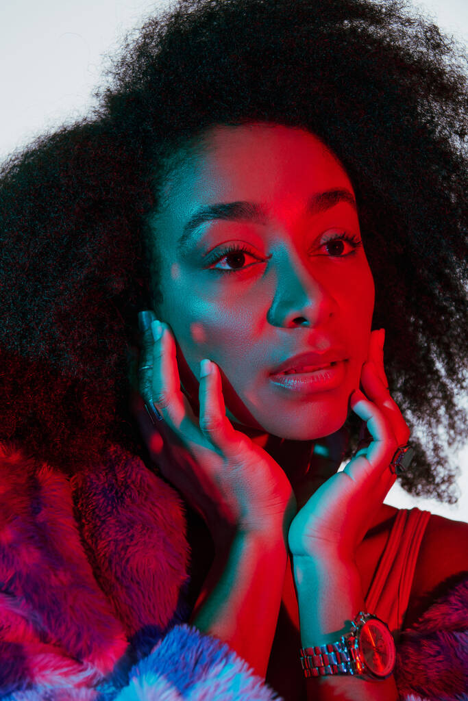 modelo femenino afroamericano atractivo en piel sintética mirando hacia otro lado en luces, concepto de moda - Foto, imagen