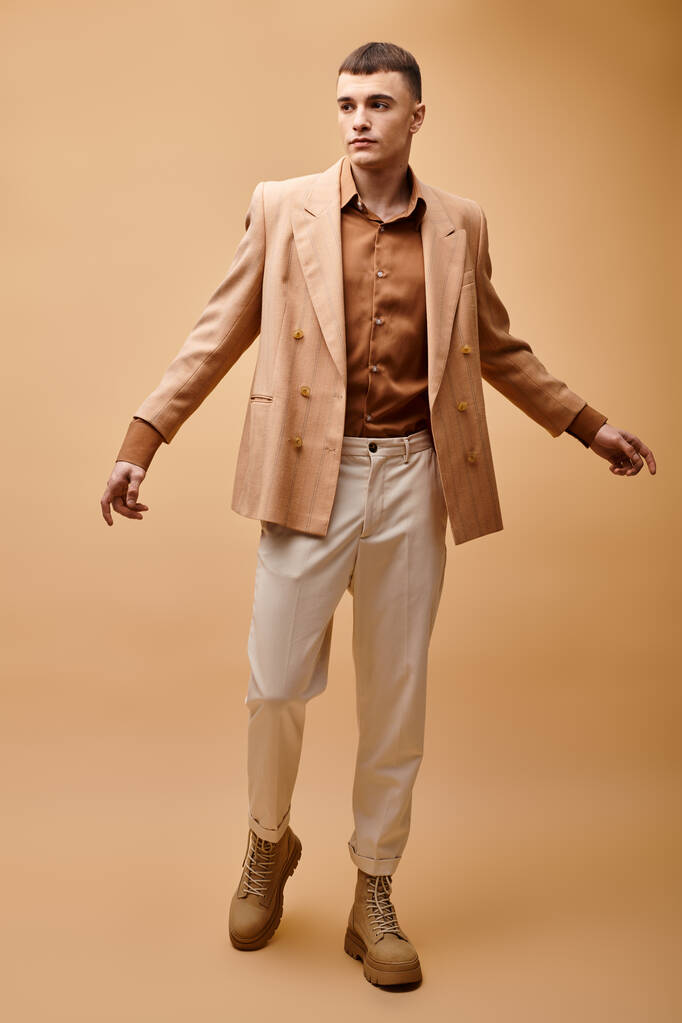 Full length portrait of fashionable man in beige jacket, shirt, pants and boots on beige background - Photo, Image