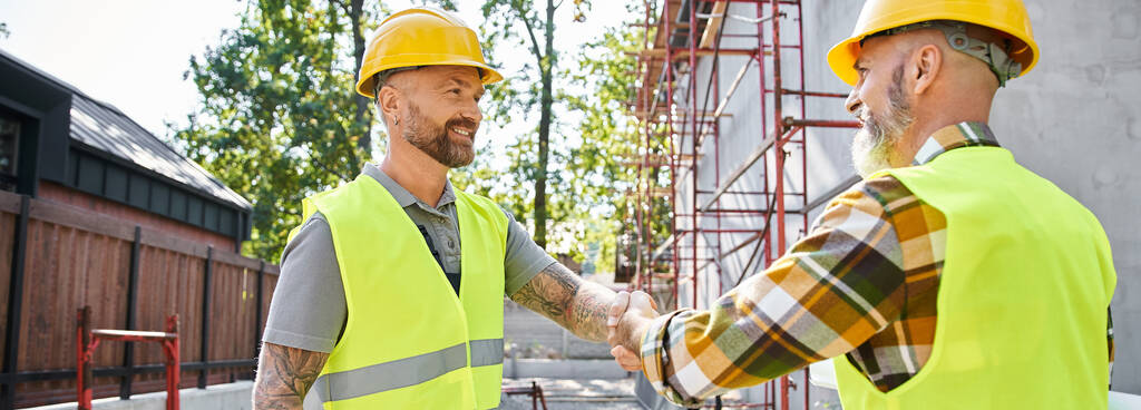 trabajadores de la construcción alegre sacudiendo sus manos y sonriendo el uno al otro, constructores de cabañas, pancarta - Foto, Imagen